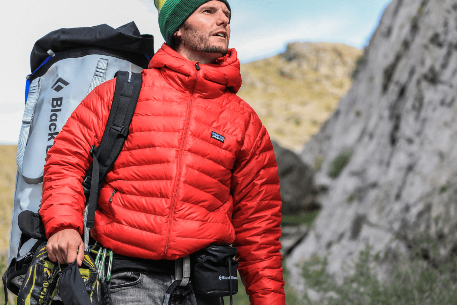 Climber wearing a red insulated jacket and backpack in a rocky mountain landscape.